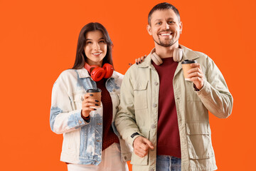 Young couple in autumn clothes with headphones and coffee cups on orange background