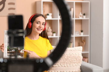 Young woman in headphones with interior design magazine recording podcast at home