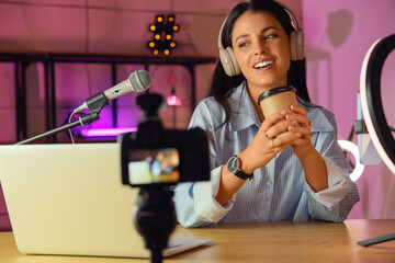 Female blogger with coffee cup recording video at home in evening