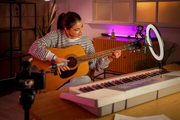Female music blogger playing guitar while recording video at home in evening