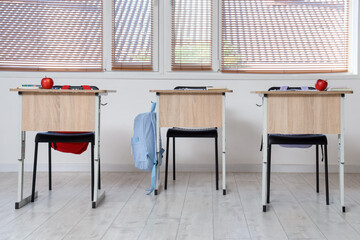 School desks with notebooks and apples in empty classroom