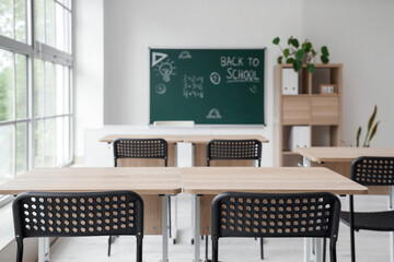Interior of empty classroom with school desks and text BACK TO SCHOOL on chalkboard