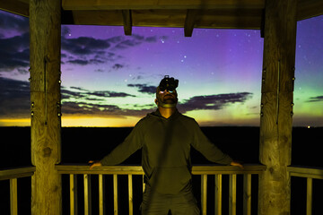 A man with a night vision binoculars on his head stands on an observation tower at night during the...