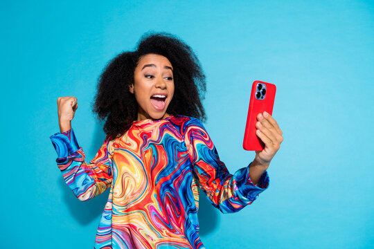 Photo portrait of pretty young girl hold device winning wear trendy colorful outfit isolated on blue color background - Powered by Adobe