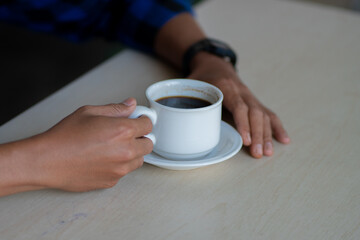 A close-up view of a person's hands gently holding a white ceramic cup of black coffee. A concept...