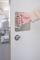 Naklejka premium Hand of an unrecognizable woman pulling the handle of the sliding door to open and exit the bathroom of a hospital room