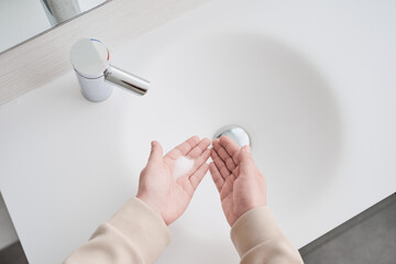 Fototapeta premium Unrecognizable woman washing hands using foaming soap in modern white bathroom sink with automatic faucet