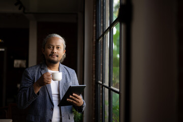 Fototapeta premium A man in a suit holding a coffee cup and looking out the window. Scene is contemplative and relaxed. lifestyle photo concept. there is copy space for ad writing 