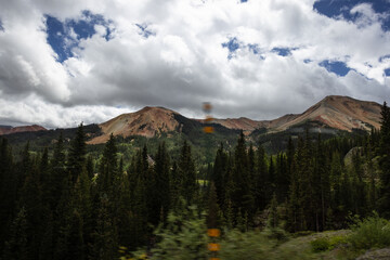 Obraz premium Photo of mountains and pine trees blue sky with white fluffy clouds taken from moving car