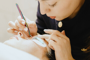 A girl cosmetologist laminates and paints the eyelashes of a teenage client.