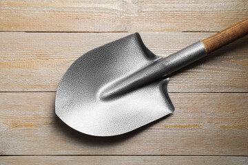 Metal shovel on light wooden table, top view