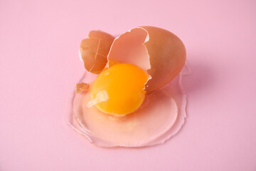 Broken raw egg with shell on pink background, closeup
