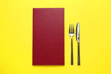 Hardcover menu and cutlery on yellow table, flat lay