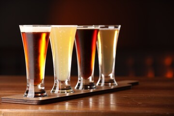 Glasses with different types of beer on wooden table against color background, closeup