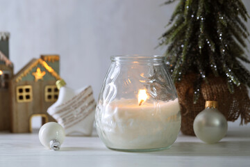 Burning candle and Christmas decor on white wooden table, closeup