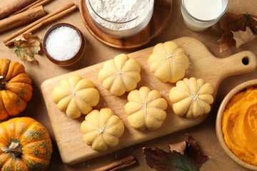 Raw pumpkin shaped buns and ingredients on brown table, flat lay