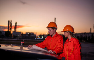 Engineers wearing safety gear, hard hats examining survey stand at car blueprint discussing on...