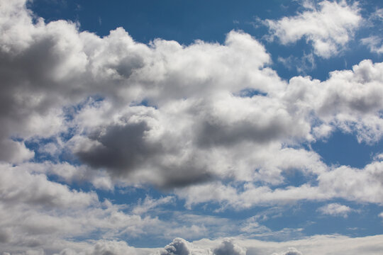 Cloud covered cloudscape photo of fluffy wispy white and grayish clouds covering a blue sky.