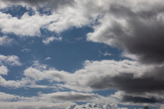 Cloudscape photograph of light and darks wispy fluffy clouds covering  a blue sky.