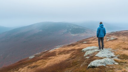 Obraz premium A lone hiker stands on a rocky ridge, gazing at mist-covered mountains in the quiet of early morning light