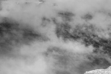 Photograph of Black and white photograph of hot steam rising from the water surface of a geyser