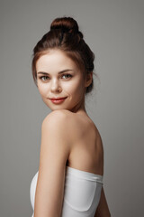 Beautiful young woman in white dress posing on a gray background