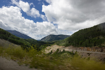Fototapeta premium Photograph taken from moving vehicle of whinnying road mountainous scenery and vivd cloudy bright blue sky in Colorado