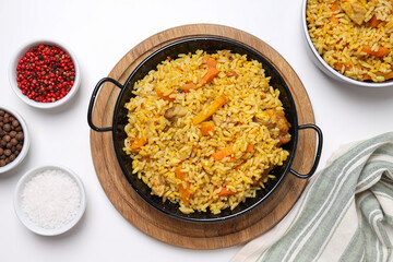 Pilaf in bowl and frying pan, spices and towel on white background, top view