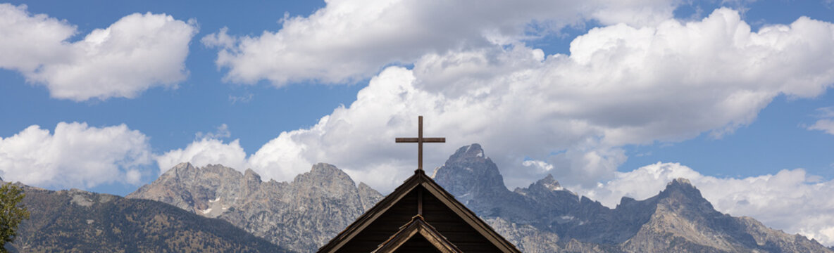 Pano cropped landscape photo of cross on top of chapel of the transfiguration overlooking the peaks of the grand Tetons Mountains. Located in the grand Tetons national park, Wyoming.