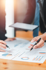 Close-up of hands holding pens and discussing financial data on charts during a business meeting.