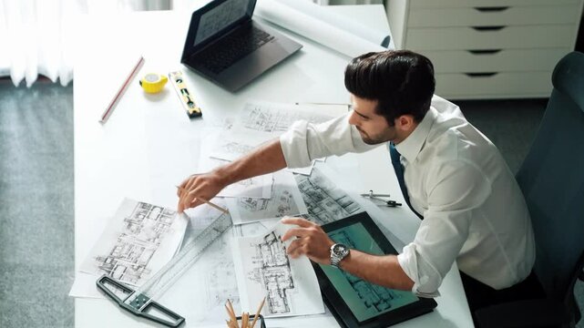 Architect engineer using laptop planning house design at office while sitting at meeting table with blueprint and equipment scatter around.Skilled civil engineer working at blueprint. Alimentation.