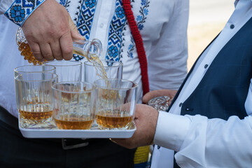 a man dressed in traditional Romanian folk costume pours brandy into glasses on a tray