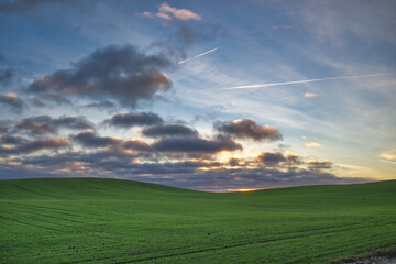 Beautiful rural landscape with green rolling fields under a dramatic sky at sunset