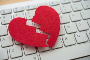 Red broken heart on white keyboard computer background. Online internet romance scam or swindler in website application dating concept. Love is bait or victim.