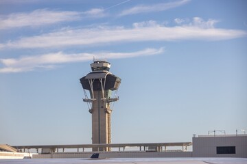 A clear view of an airport control tower against a blue sky with wispy clouds. The tower features a modern design with multiple levels and radar equipment on top.