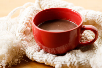 Cup of delicious hot chocolate on warm sweater on wooden table background. Selective focus.