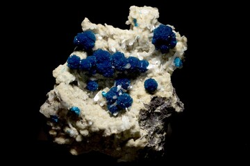 A mineral specimen featuring vibrant blue crystals clustered on a light-colored rock matrix. The contrast between the blue and the light rock creates a striking visual effect, showcasing the beauty of
