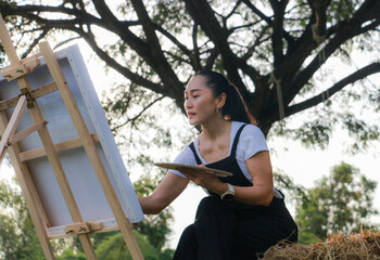 A woman sits and paints in a meadow surrounded by nature.