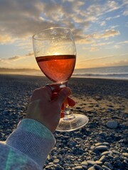 Hand holding a glass of wine with beach views and sunset at the background 