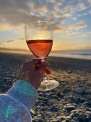 Hand holding a glass of wine with beach views and sunset at the background , glass of wine on the beach