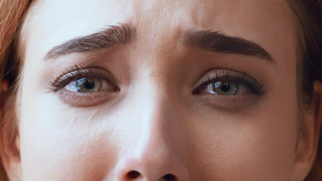 A young woman appears distressed, her blue eyes glistening with tears. The focus is on her facial expression, reflecting a moment of vulnerability and deep emotional turmoil.