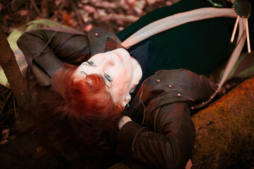 Senior lady with red vibrant hair resting on nature in autumn forest. The concept of mature woman's lifestyle
