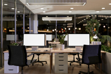 The interior design of a contemporary office in a skyscraper at night features computer desks. © bongkarn
