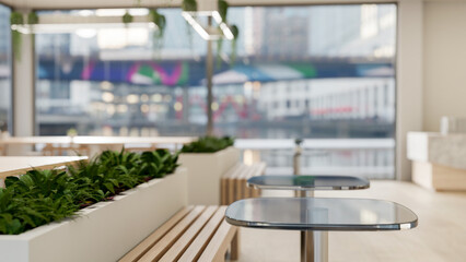 A table in a contemporary indoor setting features indoor plants, wooden benches, and a large window.
