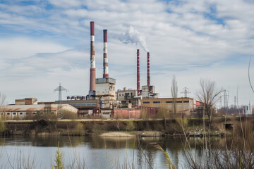 Fototapeta premium Industrial power plant with tall chimneys emitting smoke, situated near a river under a blue sky, reflecting environmental impact and urban infrastructure.