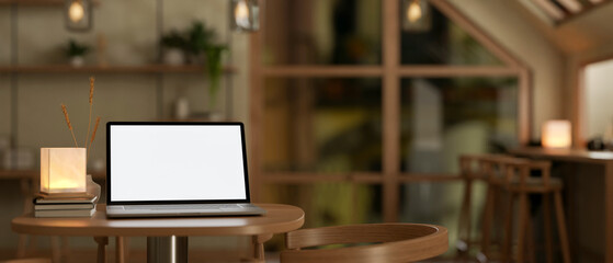 A laptop mockup sits on a wooden table in a cozy Scandinavian coffee shop at night.