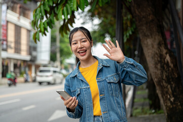 Fototapeta premium A charming Asian woman standing on a sidewalk, smiling and waving her hand at the camera.