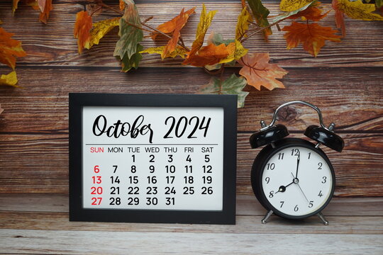 OCTOBER 2024 monthly calendar for planning and management concept with alarm clock on wooden background