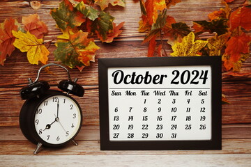 OCTOBER 2024 monthly calendar for planning and management concept with alarm clock on wooden background