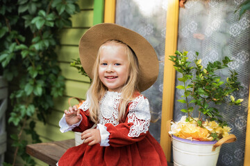 A little beautiful girl of two years old is walking in the yard. A little girl with blond hair and a hat